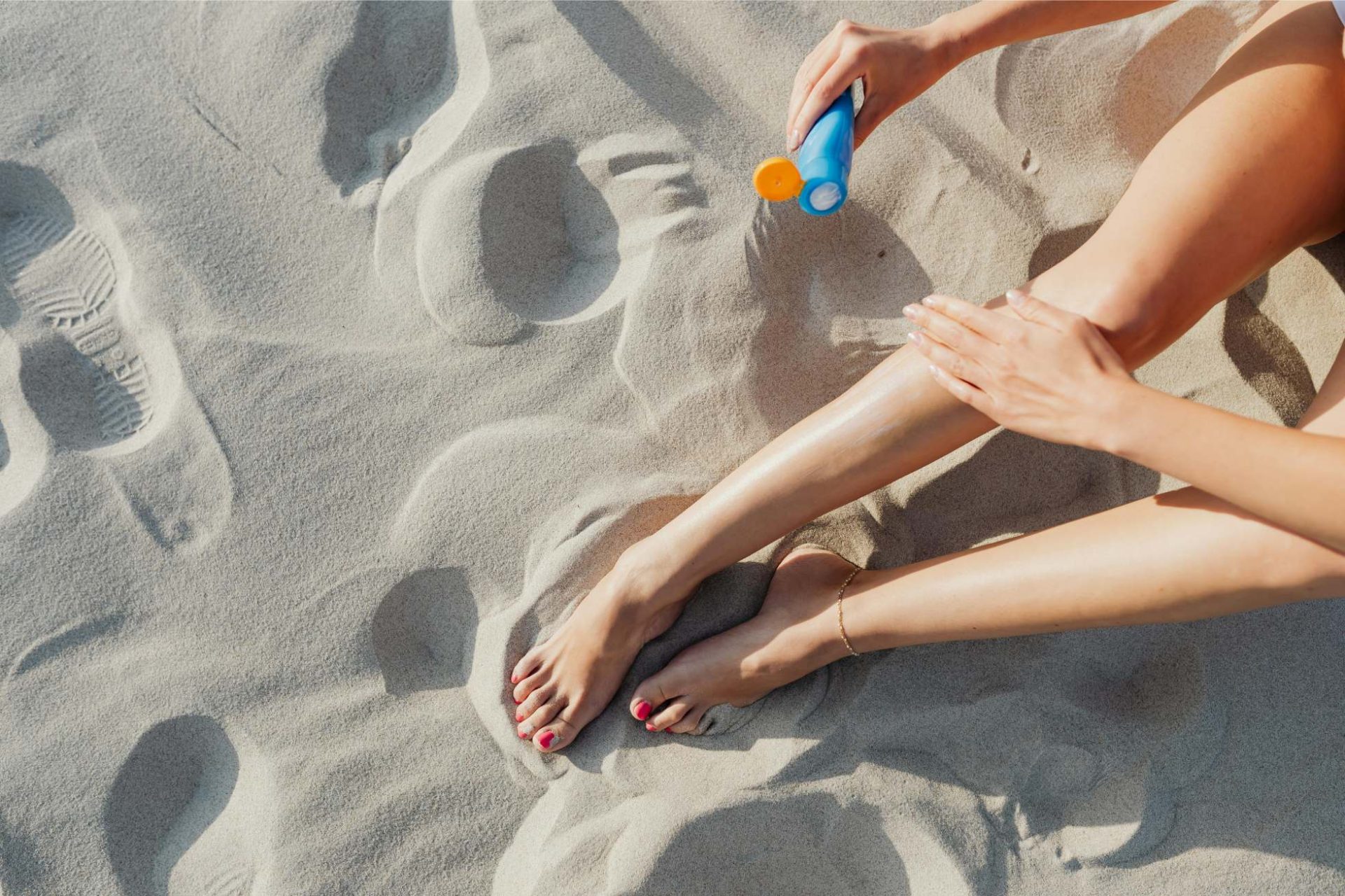 Close-up view of a person applying sunscreen lotion on legs on a sunny day at the beach.